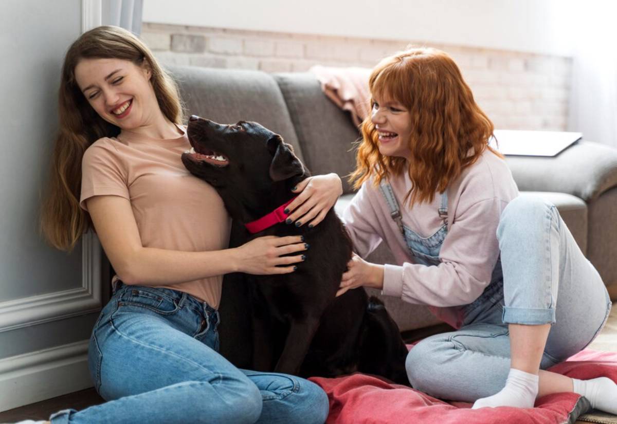 Two women playfully interact with a black dog
